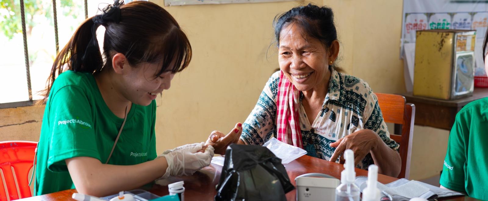 Une stagiaire de Projects Abroad mesure le taux de glycémie d'une patiente au Cambodge
